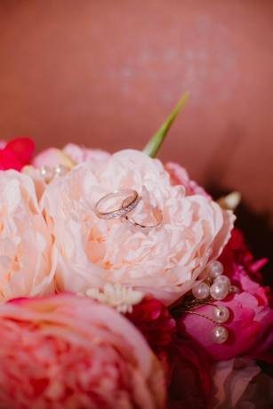 Wedding rings resting on soft pink faux peonies